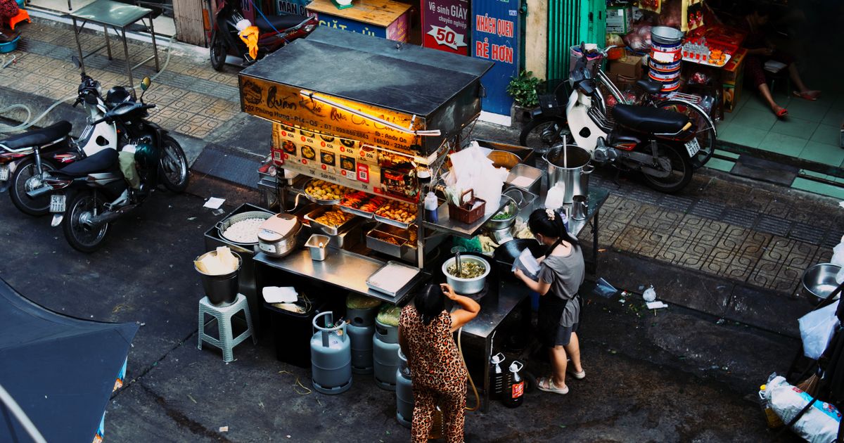 Two women preparing food at a bustling Vietnamese street food stall.