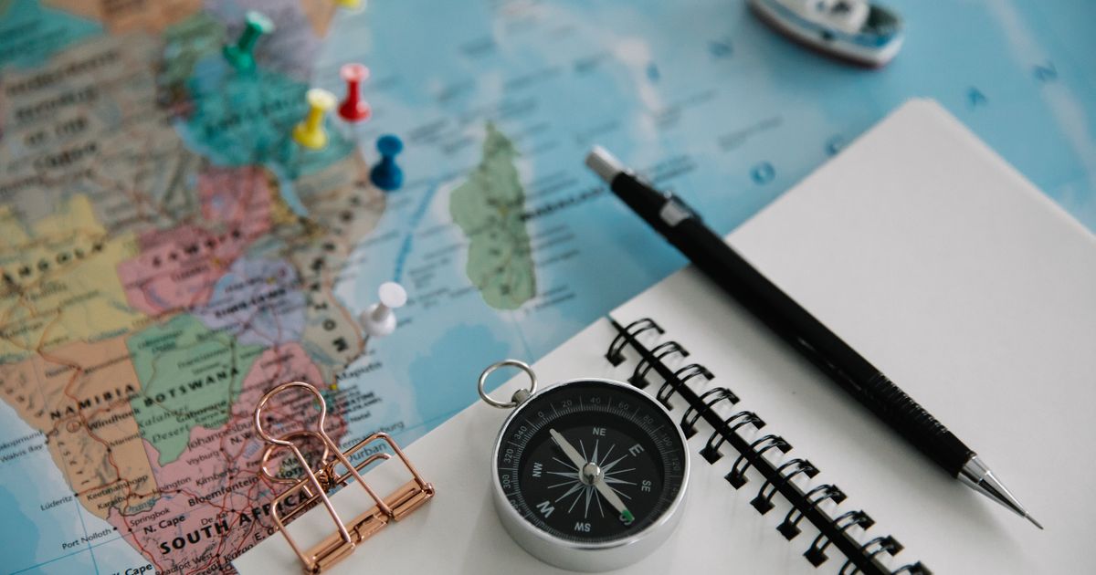 Flat lay of travel planning tools including a map, compass, notebook, and pen.