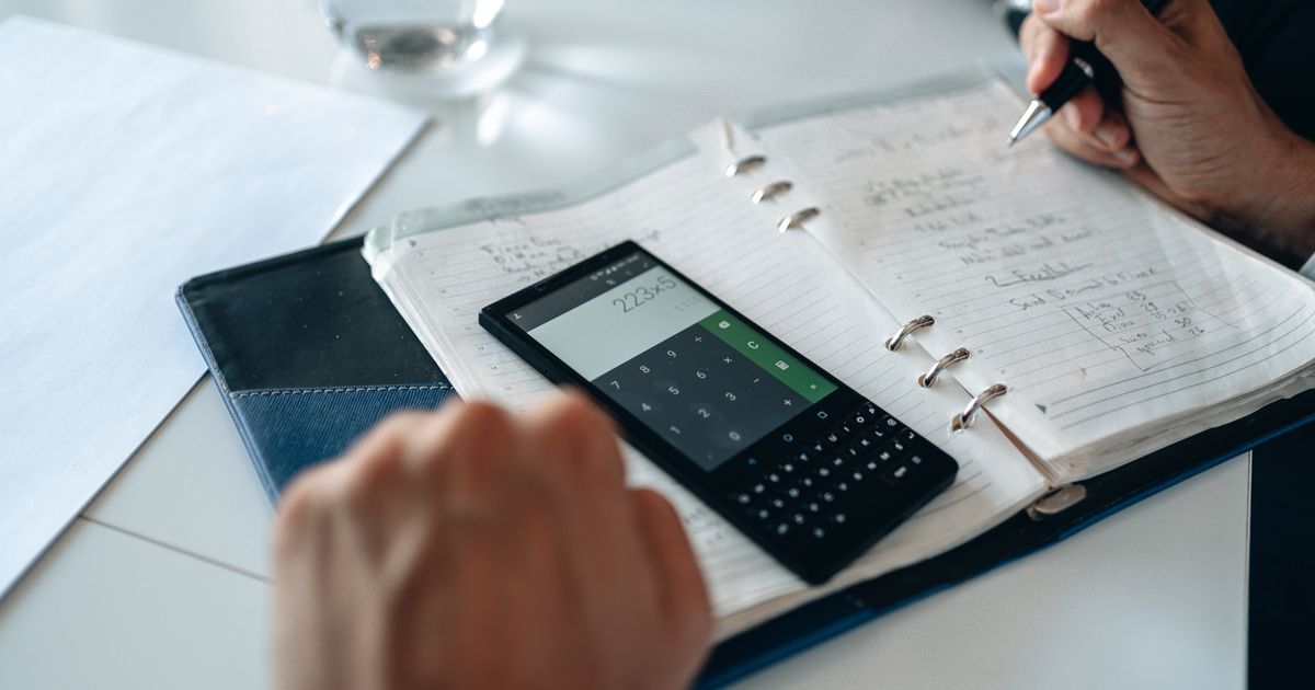 Close-up of hands writing in notebook with smartphone calculator on the table.