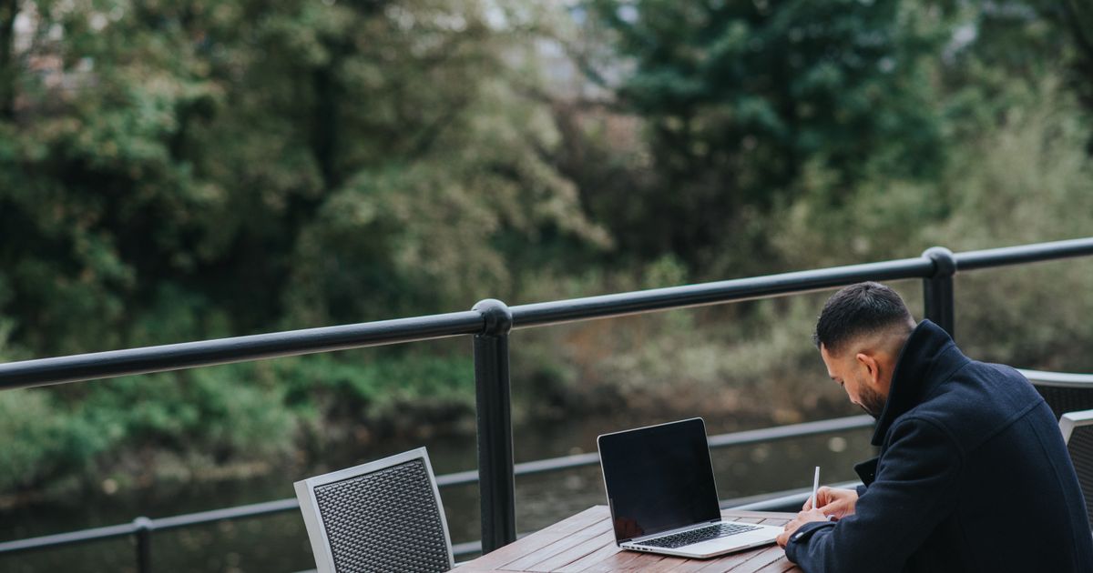 Side view of unrecognizable ethnic male executive taking notes near netbook at cafeteria table on veranda