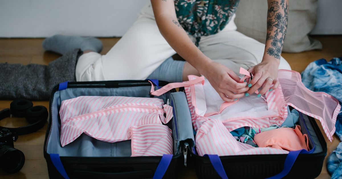 A woman packing her travel suitcase on the floor indoors, preparing for a trip.