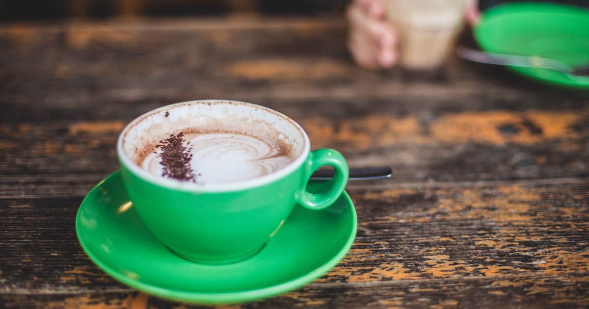 A vibrant green cup of cappuccino on a rustic wooden table with another drink in the background.